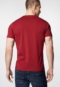 Czerwona koszulka z krótkim rękawem wykonana z bawełny, z okrągłym dekoltem i dopasowanym krojem. Widoczna logo tekstowe na górnej części pleców.