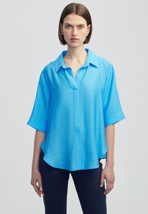Blusa azzurra a maniche corte con colletto, caratterizzata da un tessuto testurizzato e un taglio dritto, che pende liberamente dalle spalle.