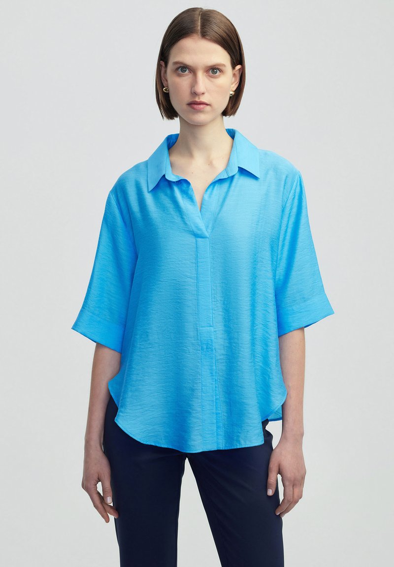 Světle modrá krátkozračka s límečkem, vyrobená z texturované látky a s rovný střih, volně visící na ramenou.