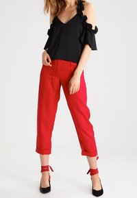 Top nero a spalle scoperte con maniche arricciate, abbinato a pantaloni rossi  cropped. Tacchi neri con lacci rossi alla caviglia completano l'outfit.