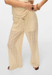 Lichtbeige gehaakte broek met wijdlopende pijpen, voorzien van een koord in de taille en complexe cirkelpatronen, met een gladde, gestructureerde afwerking.