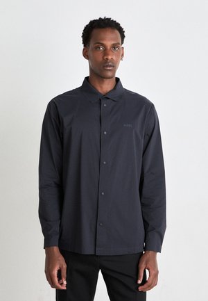 Camisa de botones azul marino con cuello clásico, mangas largas y detalle de logo. Fabricada en un tejido suave y ligero, ideal para el uso casual.