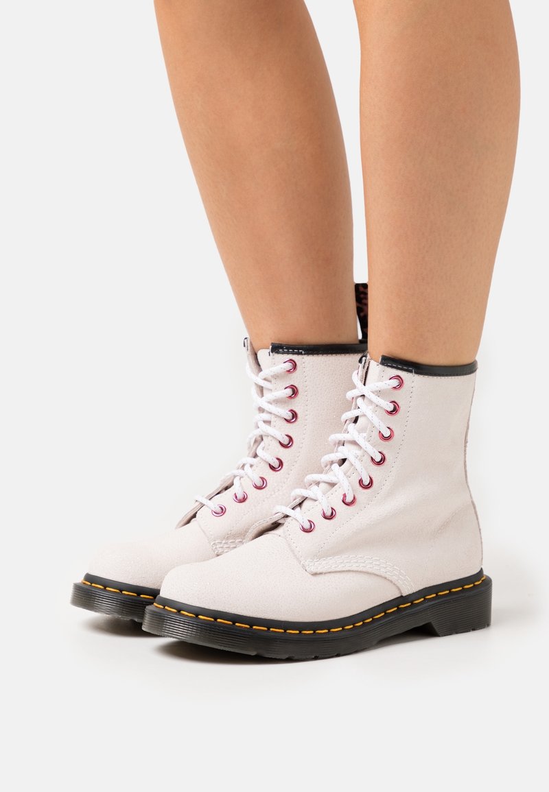 White leather ankle boots with a textured finish, black trim, red eyelets, and a contrasting yellow stitch along the sole.