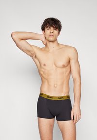 Sorte bomulls boxer briefs med en bred, gylden DIM-logo i livet, med en tettsittende design og jevn tekstur. Modellen poserer mot en enkel bakgrunn.