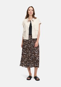 Beżowa krótka kurtka z krótkimi rękawami, czarna bluzka i brązowa plisowana spódnica w cętki. Czarne sandały dopełniają całość.