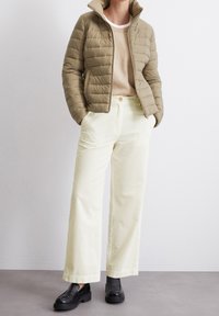 Khaki pufferjack met een rits, beige gebreid trui, crèmekleurige corduroy wide-leg broek en zwarte platform schoenen. Gestructureerde materialen, casual pasvorm.