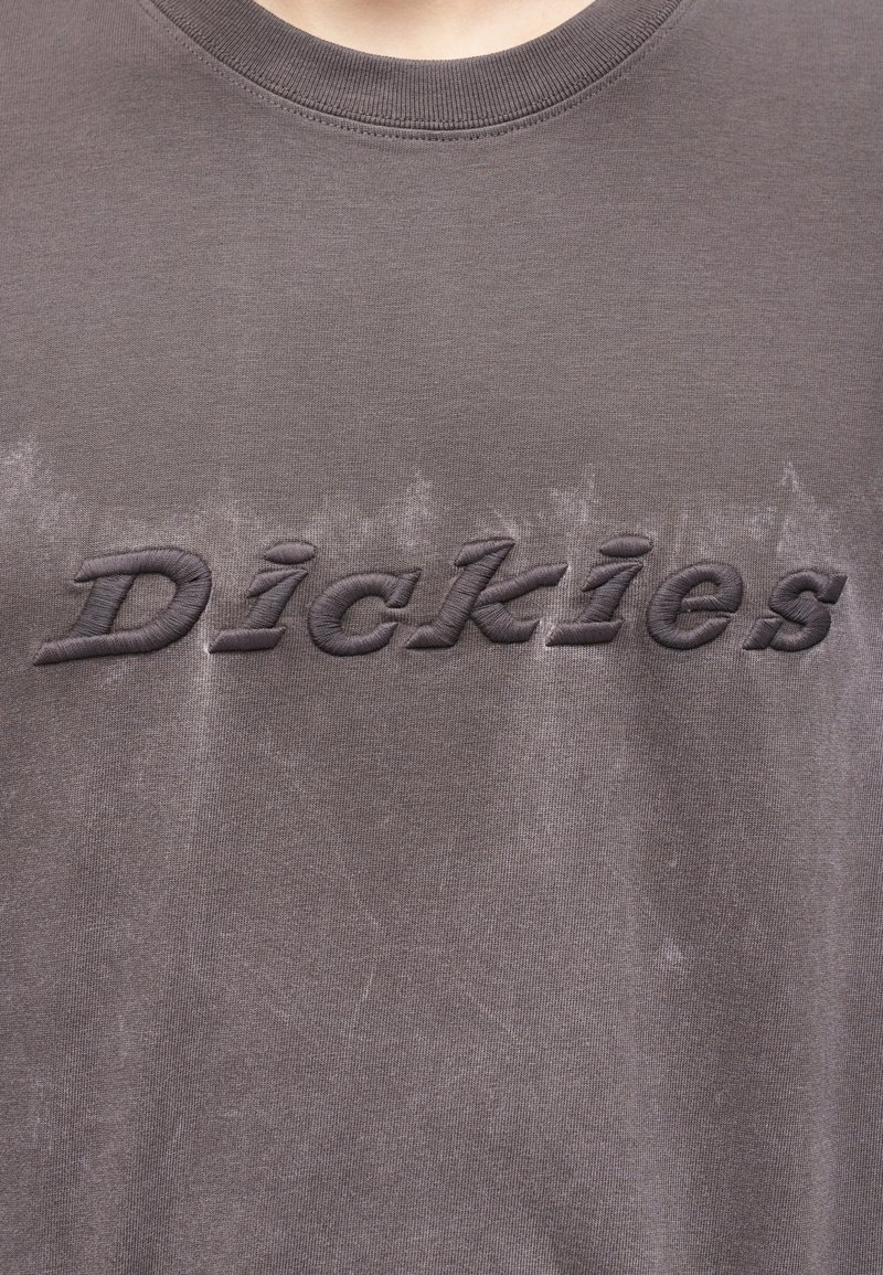 Primo piano di una maglia grigia con collo a giro, con il nome del marchio "Dickies" ricamato sul petto con filo dello stesso colore.