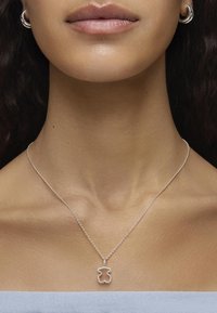 Srebrny naszyjnik z zawieszką w kształcie niedźwiedzia, z cienkim łańcuszkiem i eleganckim, minimalistycznym designem na tle w neutralnych odcieniach.