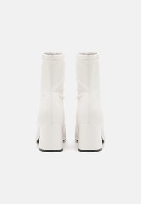 Bottines blanches avec une finition lisse, bout rond et un talon épais. Présente une texture froncée et une semelle noire contrastante.