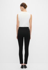 Pantalons noirs ajustés avec une texture lisse et des coutures verticales ; associés à un haut sans manches blanc. Portés avec des chaussures noires.