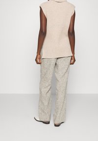 Top senza maniche a coste beige abbinato a pantaloni larghi in tessuto grigio chiaro, con orlo posteriore leggermente più lungo e un motivo sottile.