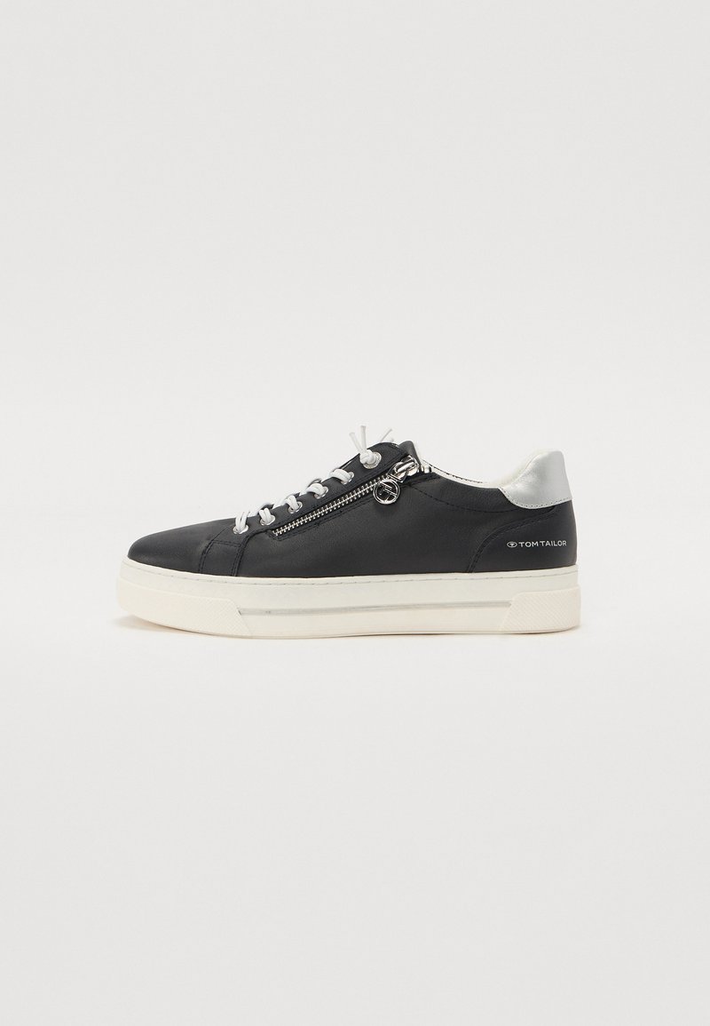 Baskets en cuir noir avec semelle blanche, présentant un accent argenté à l'arrière, des lacets contrastants et un détail de fermeture éclair sur le côté.