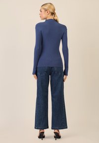 Top a coste blu con maniche lunghe, silhouette aderente; abbinato a jeans di denim a vita alta con gamba larga e dettagli ricamati.