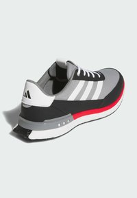 Szary but sportowy z czarnymi akcentami, trzema białymi paskami, czerwoną podeszwą środkową, teksturowaną siateczkową cholewką i płaskimi białymi sznurowadłami. Zaokrąglony nosek i wyściełany kołnierz.