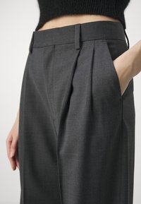 Pantalons gris ajustés avec taille haute, plis à l'avant et poches latérales, en tissu lisse et texturé.