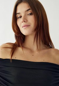 Čierny top bez ramienok s textúrovanou tkaninou, ktorý má jemné drapérie a elegantný dizajn. Hladký výstrih a mäkký, splývavý materiál.