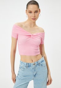 Rosa ribbad off-shoulder crop top med vriden framdel, parat med ljusblå höga slitna jeans.