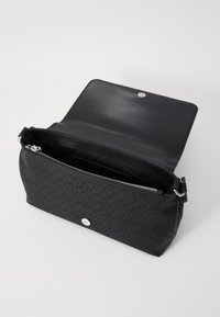 Zwarte stoffen handtas met geometrisch patroon, zilverkleurige hardware en ritsafsluiting. Beschikt over een gladde leren interieur en een verstelbare hengsel.
