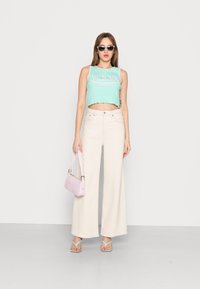 Top de alças mint cropado com bainha em ondulação, combinado com calças largas de cintura alta em bege. Uma bolsa rosa clara e sandálias verde pastel completam o visual.