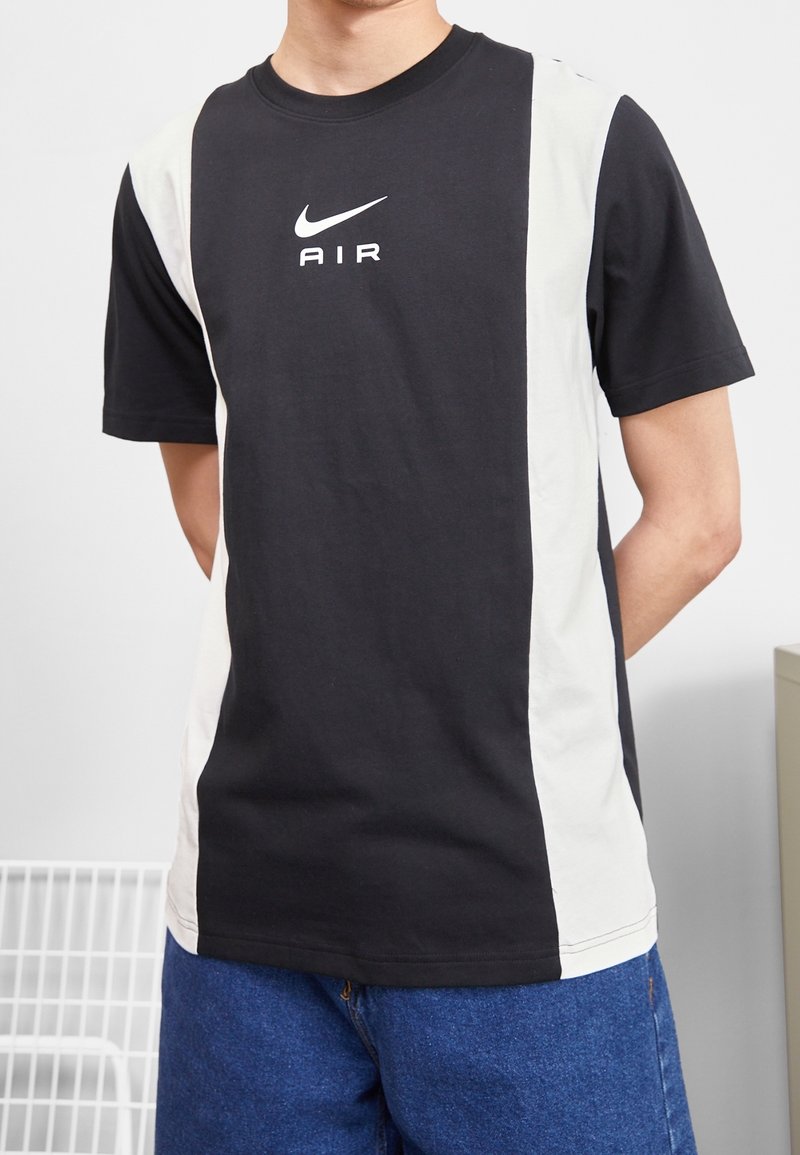 Schwarzes kurzärmliges T-Shirt mit weißen Seitenpaneelen, das ein weißes Nike-Logo in der Mitte trägt. Hergestellt aus Baumwolle mit glatter Textur.