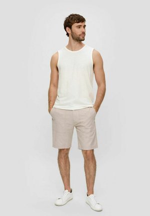 Weißes ärmelloses Tanktop kombiniert mit hellbeigen Shorts. Die Shorts haben zwei Fronttaschen und sind mit weißen Sneakers kombiniert.