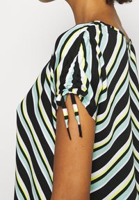 Blouse à rayures noir et blanc avec des accents bleu clair et jaune ; possède des manches froncées avec des attaches ; texture de tissu lisse.