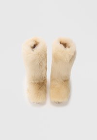 Stivali beige pelosi realizzati in materiale morbido, con forma arrotondata e parte superiore aperta, caratterizzati da una texture soffice. Nessun hardware o motivo visibile.