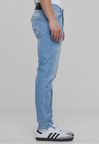 Svijetloplavi traperice slim fit kroja, s mid-rise strukom, sitnim izblijedjenjima i detaljima na stražnjem dijelu. Uparene s bijelim tenisicama.