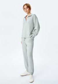 Lichtgrijze sweatshirt met een half-rits kraag en verlaagde schouders, gecombineerd met bijpassende joggers met een elastische tailleband en boorden.