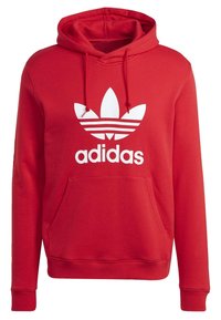 Červená mikina Adidas s kapucí a bílým logem trefoil, s předními klokaními kapsami, nastavitelnou kapucí se stahovací šňůrkou a dlouhými rukávy.