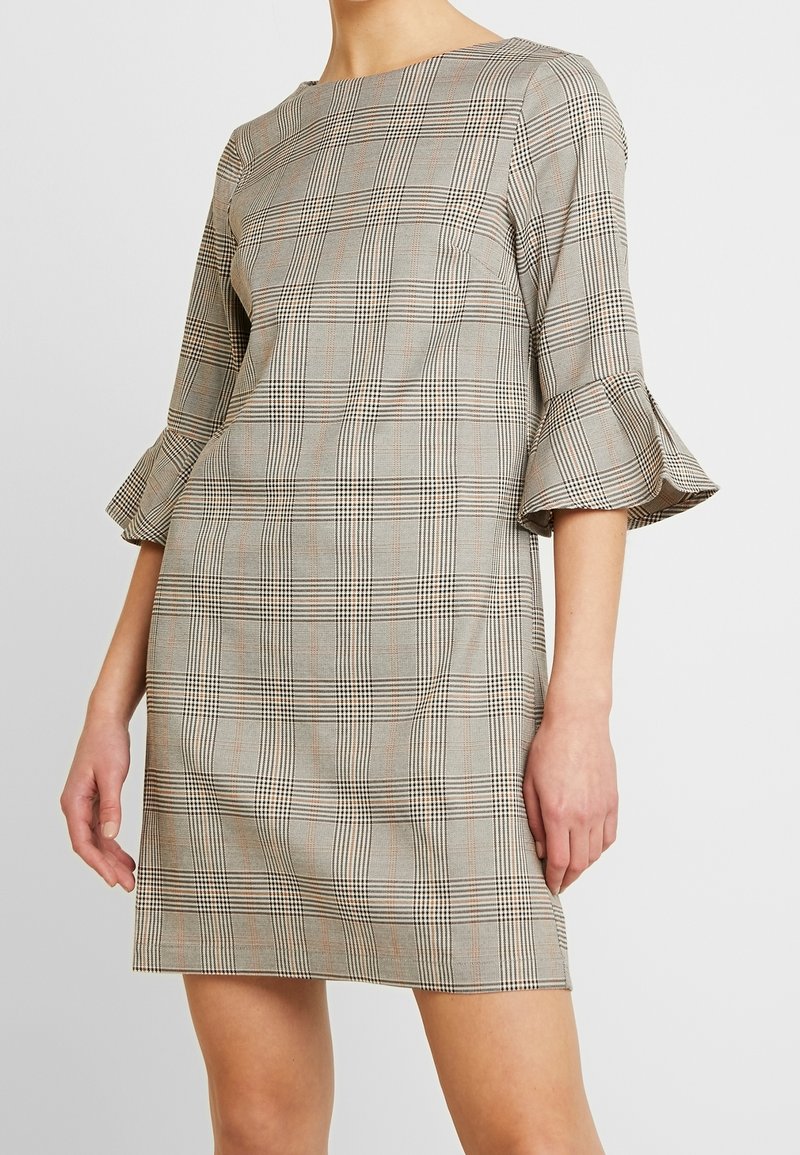 Rutiga klänningen i beige och svart med volangärmar, har rak skärning och rund halsringning, tillverkad av en texturerad tyg.