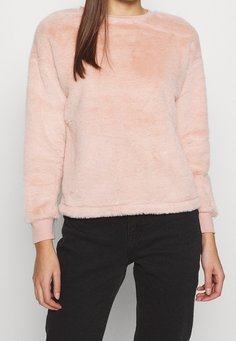 Sweat-shirt en polaire rose clair avec encolure ronde et manches longues. Texture douce, détails côtelés aux poignets et à l'ourlet, et coupe décontractée.