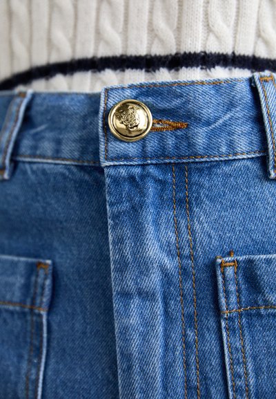 Modri denim kavbojki z zlatim gumbom na pasu, z vidnim šivanjem in sprednjimi žepi. Tkanina ima gladko teksturo.