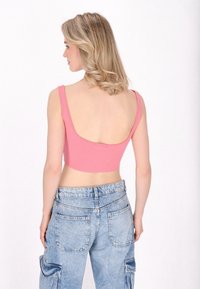Top corto rosa con spalline larghe, schiena a barchetta, indossato con jeans cargo in denim azzurro chiaro a vita alta con tasche laterali.