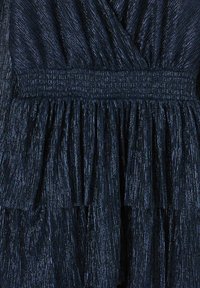 Robe bleu marine avec des rayures métalliques verticales, présentant une taille smockée et une jupe épaulée à volants pour texture et mouvement.