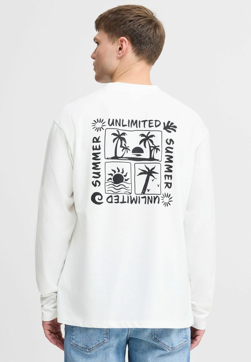 Camiseta blanca de manga larga con diseño gráfico negro que presenta palmeras y motivos del sol, el texto dice "VERANO ILIMITADO", corte relajado.
