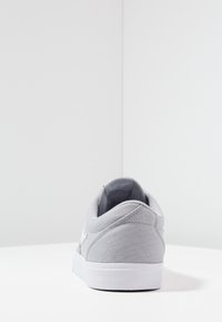 Grå canvas sneakers med låg profil, vit gummisula, vadderad krage och en diskret logotyp på sidan. Slät yta genom hela skon.