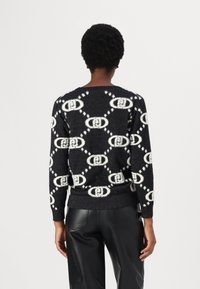 Zwart-wit geblokte trui met een logo ontwerp, voorzien van een zachte textuur, geribde manchetten en zoom, gecombineerd met zwarte broek.