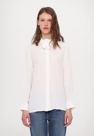 Camicia bianca a maniche lunghe con un dettaglio testurizzato a forma di rosa sul colletto, dotata di chiusura con bottoni e realizzata in un tessuto liscio e leggero.