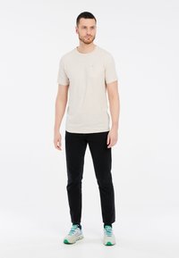 Beżowa koszulka z krótkim rękawem z kieszonką na piersi, zestawiona z czarnymi, dopasowanymi spodniami oraz wielokolorowymi butami sportowymi. Prosty, casualowy styl.