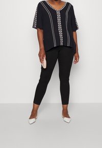 Svart kortärmad topp med vit blommig broderi längs halsringningen och sidorna, i kombination med svarta leggings och vita spetsiga ballerinas.