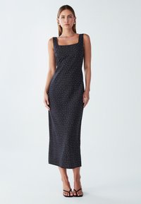 Crna, uska midi haljina sa četvrtastim dekolteom, bijelim točkicama i glatkom teksturom. Ima tanke naramenice i ravni rub.