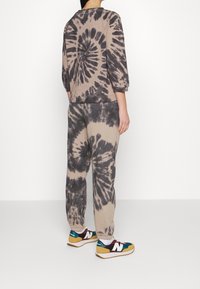 Beige tie-dye sweatshirt med trekvart ärmar som matchas med joggers. Sneakers har flerfärgade detaljer och vita snören.