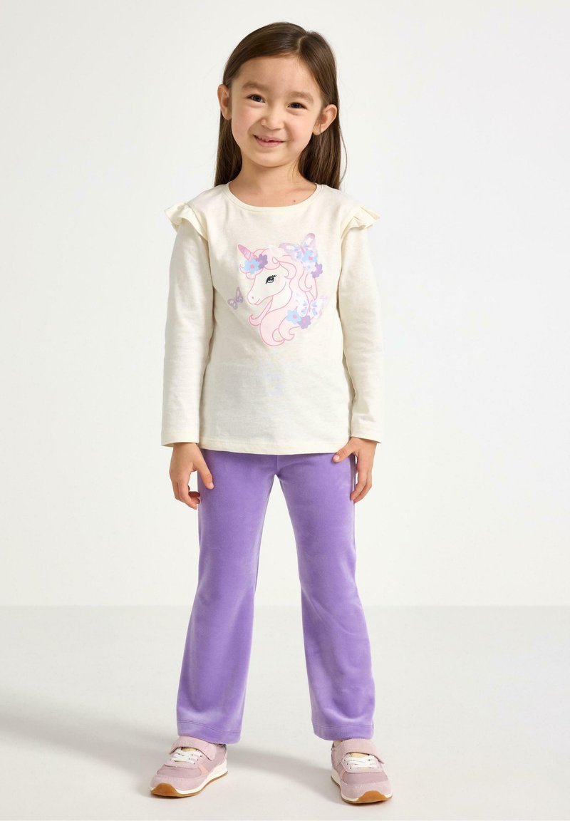Light cream long-sleeve shirt with ruffled sleeves and unicorn graphic, paired with soft purple pants and light pink sneakers.