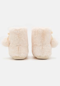Pink plush slippers with a soft, fuzzy texture, featuring rounded tops, a small pom-pom accent, and a ribbon detail on the back.