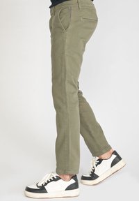 Pantalons vert olive avec une coupe slim, comprenant des poches avant, une poche arrière et des détails cousus ; associés à des baskets noir et blanc.