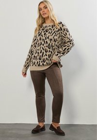 Beige tröja med svart och brun leopardmönster, rund halsringning, löst sittande; matchad med bruna mocka-liknande byxor och mörka loafers.