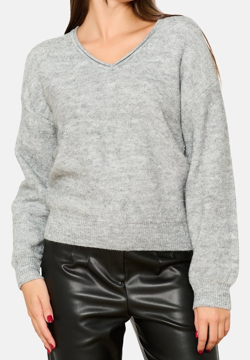 Grauer Strickpullover mit V-Ausschnitt, gerippten Bündchen und Saum. Weiche Textur mit dezentem Schimmer. Kombiniert mit schwarzen Kunstlederhosen.