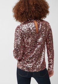 Top a maniche lunghe in oro rosa con paillettes, caratterizzato da una schiena a occhiello. Presenta paillettes rotonde su tutta la superficie e una silhouette aderente. Texture morbida.