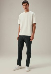 Weißes T-Shirt mit kurzen Ärmeln, kombiniert mit dunkelgrünen Hosen und weißen Sneakers. Einfaches Design, aus Baumwolle und lässiger Schnitt.